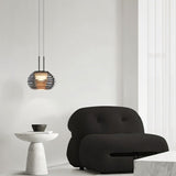 "Smoky grey Filano pendant light with ribbed glass shade and iron frame, hanging above a modern armchair and side table."