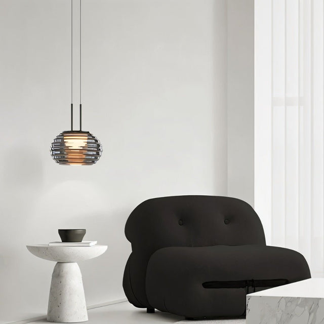 "Smoky grey Filano pendant light with ribbed glass shade and iron frame, hanging above a modern armchair and side table."
