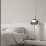 "Smoky grey Filano pendant light with a smooth glass shade and iron frame, hanging above a bed in a minimalist bedroom."