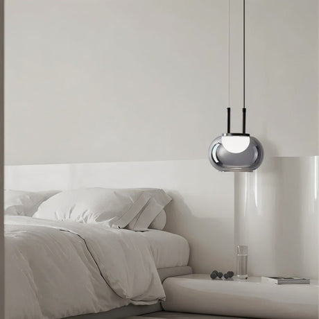 "Smoky grey Filano pendant light with a smooth glass shade and iron frame, hanging above a bed in a minimalist bedroom."