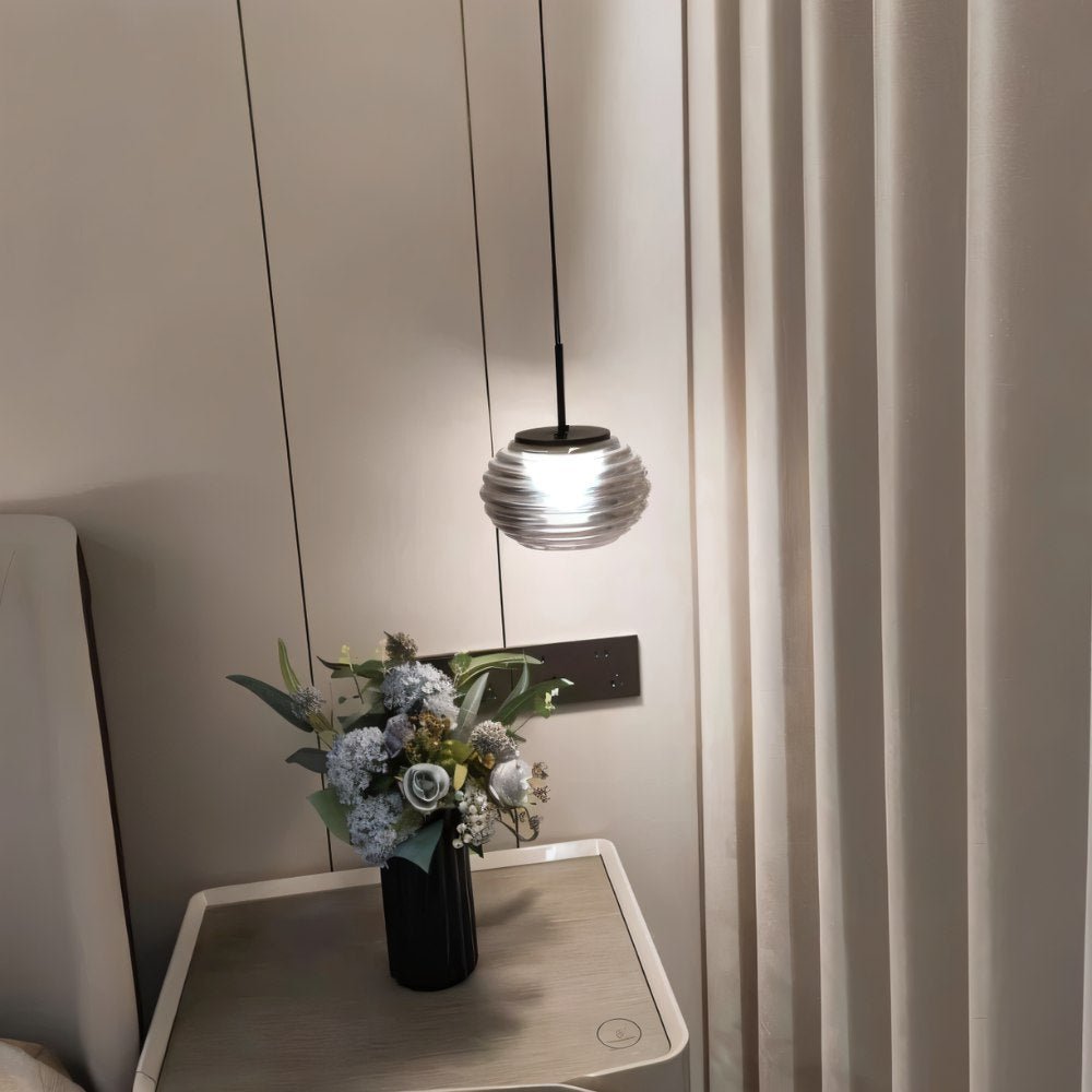 "Smoky grey Filano pendant light with ribbed glass shade and iron frame, hanging above a bedside table with a flower arrangement."