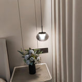 "Smoky grey Filano pendant light with ribbed glass shade and iron frame, hanging above a bedside table with a flower arrangement."