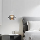 "Smoky grey Filano pendant light with a ribbed glass shade and iron frame, hanging above a bedside table in a bedroom."
