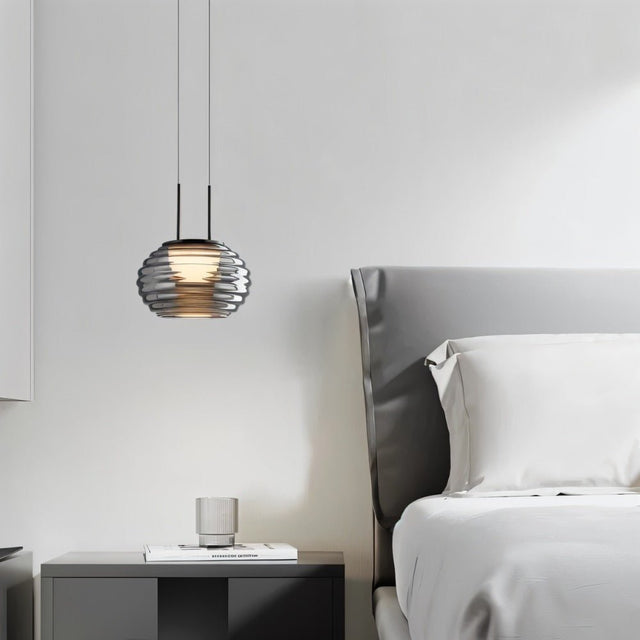 "Smoky grey Filano pendant light with a ribbed glass shade and iron frame, hanging above a bedside table in a bedroom."