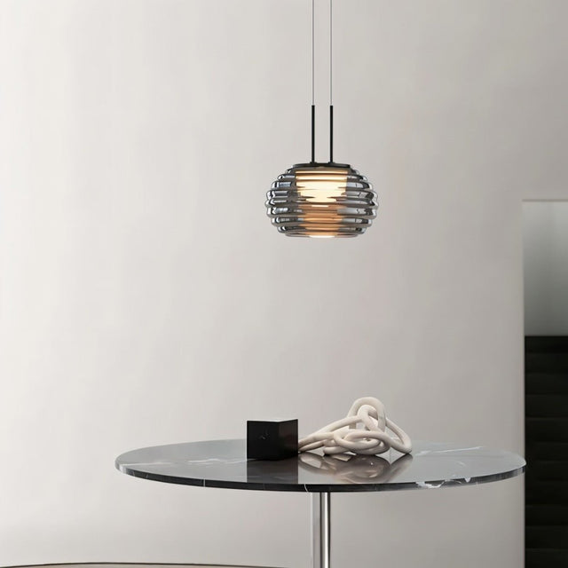 "Smoky grey Filano pendant light with ribbed glass shade and iron frame, hanging above a marble table with decorative objects."