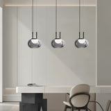 "Three smoky grey Filano pendant lights with smooth glass shades and iron frames, hanging above a desk in a modern interior."