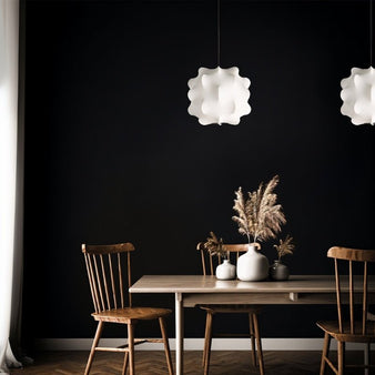 "Pair of white pendant lights with cloud-like shades hanging over a rustic dining table with wooden chairs against a dark wall."