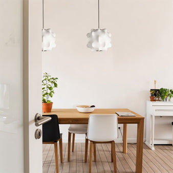 "Pair of white pendant lights with cloud-like shades hanging over a minimalist dining table with chairs and a plant."