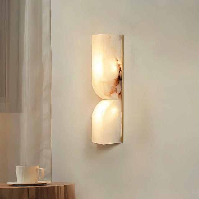 "A double curved alabaster wall lamp providing soft lighting in a bedroom setting."