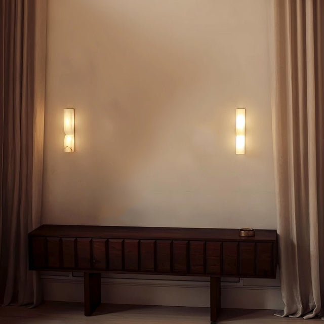 "Two double curved alabaster wall lamps flanking a console in a living room, providing ambient lighting."