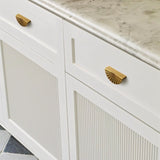 "Vintage brass fan-shaped drawer pulls with a ridged, pleated surface, installed on white bathroom drawers with grooved detailing, adding a touch of Art Deco elegance to the space."