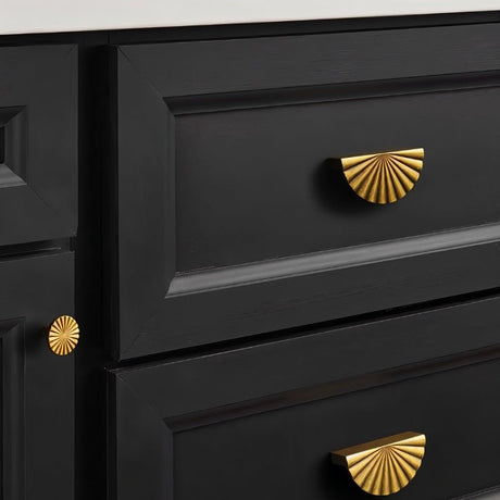 "Vintage brass fan-shaped drawer pulls with a ridged, pleated surface and intricate grooves, installed on black kitchen drawers, adding a touch of Art Deco inspiration to the space."