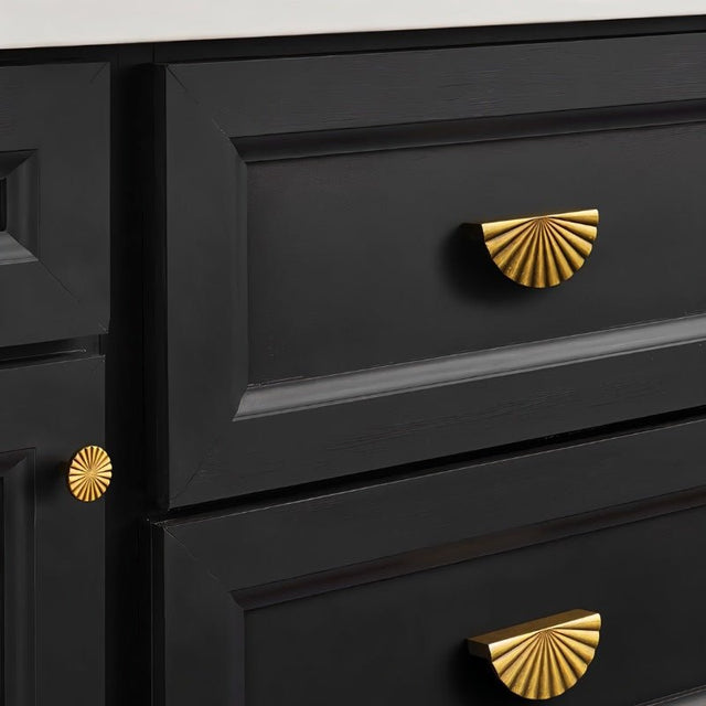 "Vintage brass fan-shaped drawer pulls with a ridged, pleated surface and intricate grooves, installed on black kitchen drawers, adding a touch of Art Deco inspiration to the space."