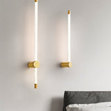  "Two modern wall sconces with long, thin light bars and brass accents, mounted on either side of a bed in a minimalist bedroom."