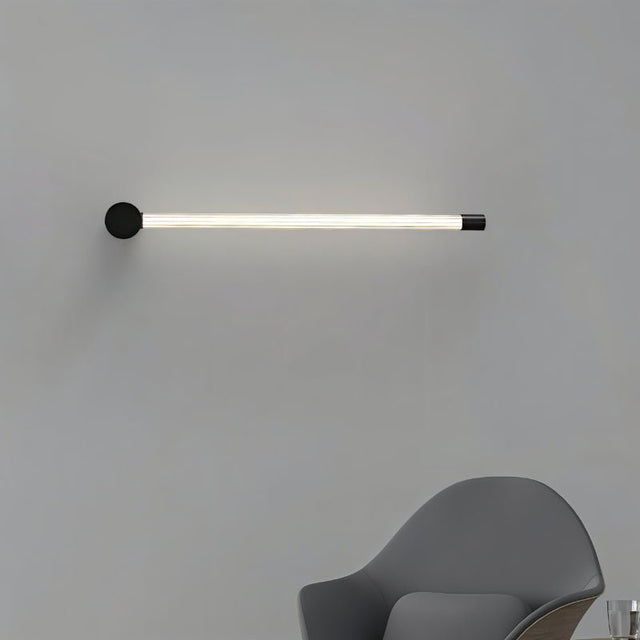 "A sleek, horizontal black wall sconce with a long, thin light bar and acrylic diffuser, mounted on a gray wall above a chair."