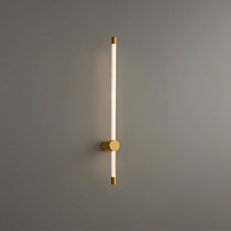 "A sleek, vertical brass wall lamp with a long, thin light bar and acrylic diffuser, mounted on a gray wall in a modern bathroom."