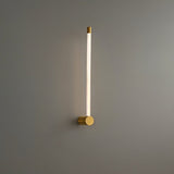 "A modern brass wall lamp with a long, thin light bar and acrylic diffuser, mounted vertically on a gray wall in a bathroom setting."