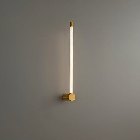 "A modern brass wall lamp with a long, thin light bar and acrylic diffuser, mounted vertically on a gray wall in a bathroom setting."