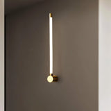 "A sleek, vertical brass wall sconce with a long, thin light bar and acrylic diffuser, mounted on a gray wall."