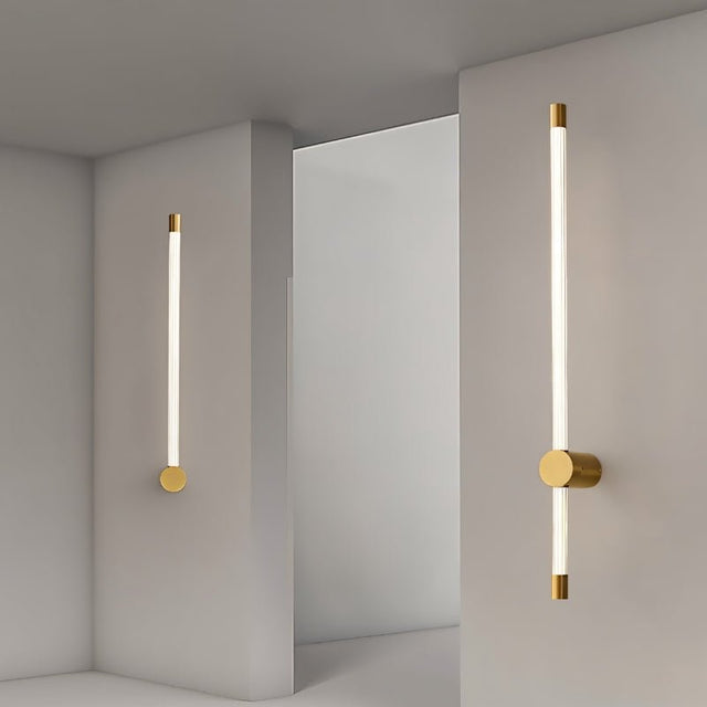 "Two modern wall lamps with long, slender light bars and brass accents, illuminating a minimalist hallway."