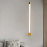 "A modern, linear wall lamp with a brass finish and acrylic diffuser, mounted vertically on a light gray wall in a living room."