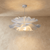 White sculptural petal pendant light with warm glow hanging above bedroom with dark accent wall and upholstered headboard.