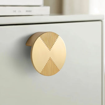 "Close-up of a brass cabinet knob with a bold circular design and etched geometric detailing."