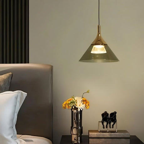 "A modern pendant light with a conical gray shade and gold top, hanging above a nightstand with flowers and decorative figures."