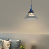 "A modern pendant light with a conical gray shade and blue top, hanging above a bed with pillows and a glass dome."