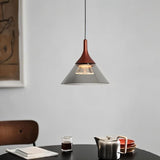"A modern pendant light with a conical gray shade and rust-colored top, hanging above a dining table with a teapot and dishes."