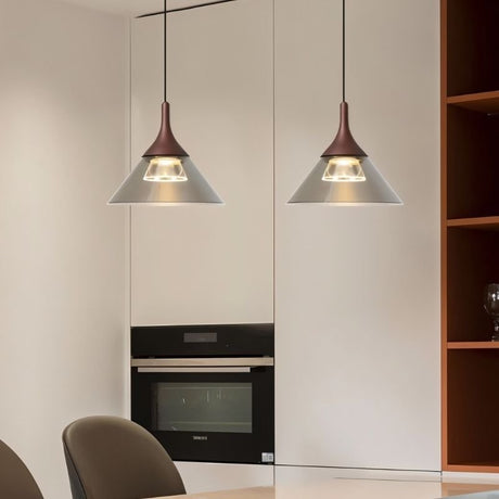 "Two modern pendant lights with conical gray shades and rust-colored tops, hanging over a kitchen counter with a built-in oven."