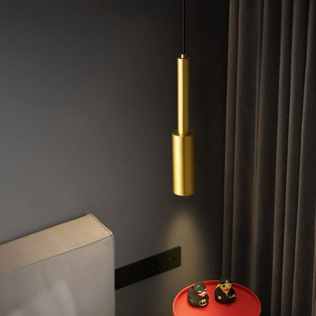 "Minimalist brass pendant light with a slender, cylindrical design, casting a focused light on a modern bedroom nightstand, enhancing ambiance and providing task lighting."