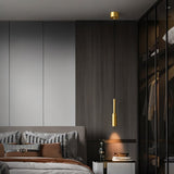 "Minimalist brass pendant light with a slender, cylindrical design, providing a focused light in a modern bedroom setting, highlighting the clean lines and contemporary aesthetic."