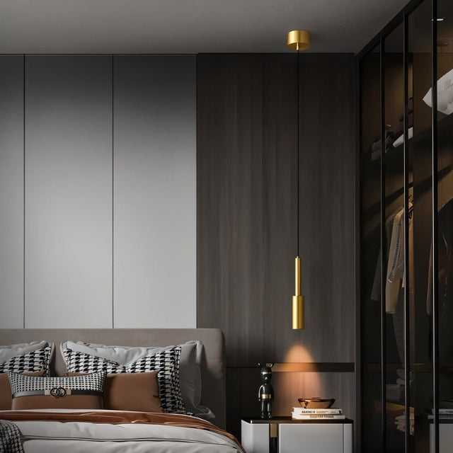 "Minimalist brass pendant light with a slender, cylindrical design, providing a focused light in a modern bedroom setting, highlighting the clean lines and contemporary aesthetic."