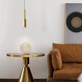 "Minimalist brass pendant light with a slender, cylindrical design, casting a focused light in a modern living room setting, complementing a round side table with a decorative sculpture."