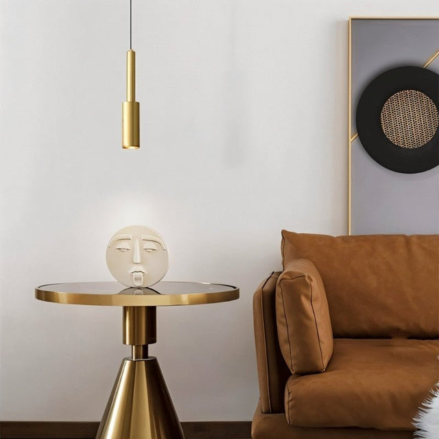 "Minimalist brass pendant light with a slender, cylindrical design, casting a focused light in a modern living room setting, complementing a round side table with a decorative sculpture."