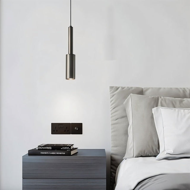 "Minimalist iron pendant light with a slender, cylindrical profile, providing focused downward illumination as a bedside reading light in a modern bedroom."