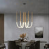 Modern brass tube chandelier with curved white LED tubes suspended over a dining table with chairs.