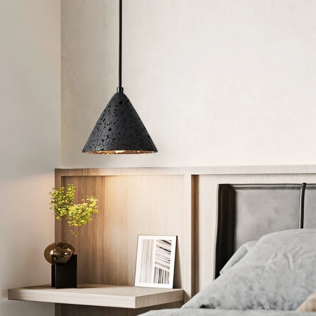 "A conical black travertine pendant light hanging above a bedside table in a modern bedroom, providing ambient lighting."