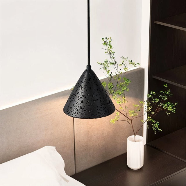 "A close-up of a conical black travertine pendant light hanging in a bedroom, showing the stone's texture."