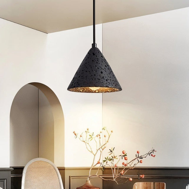 "A conical black travertine pendant light hanging above a dining table, illuminating the space with a warm light."