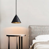 "A conical black travertine pendant light hanging above a bedside table, emitting a warm glow in a bedroom."