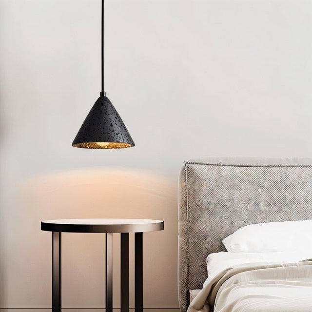 "A conical black travertine pendant light hanging above a bedside table, emitting a warm glow in a bedroom."