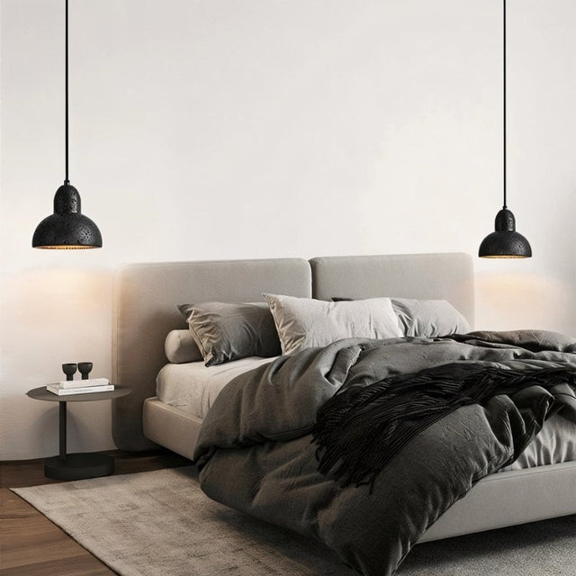 "Two domed black travertine pendant lights hanging above a modern bed in a minimalist bedroom."