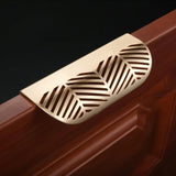 "A close-up of a gold leaf-shaped drawer pull on a dark wood cabinet."