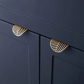 "Two gold leaf-shaped drawer pulls on a dark blue kitchen cabinet."