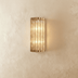 Gold ribbed cylindrical wall sconce with warm light on bathroom vanity mirror, lifestyle setting.