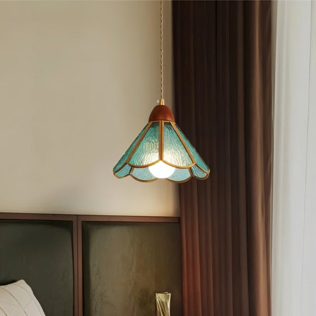 "Handcrafted blue glass pendant light with copper trim hanging in a bedroom setting, providing a warm, ambient glow."