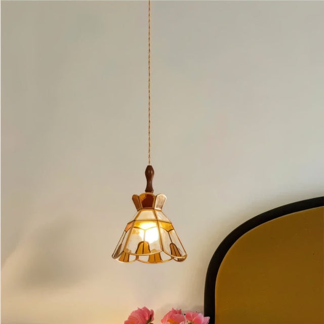"Handcrafted vintage-style pendant light with amber stained glass hanging in a bedroom, casting a warm glow."