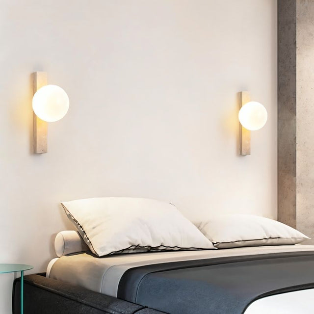 "Modern travertine wall lamps with frosted glass globes installed on both sides of a bed"